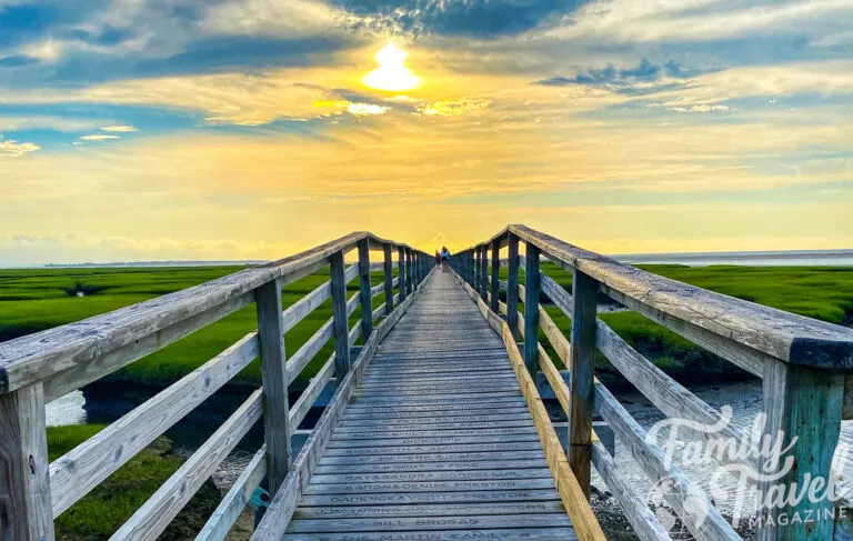 Long wooden pier over marshes at sunset with orange sky