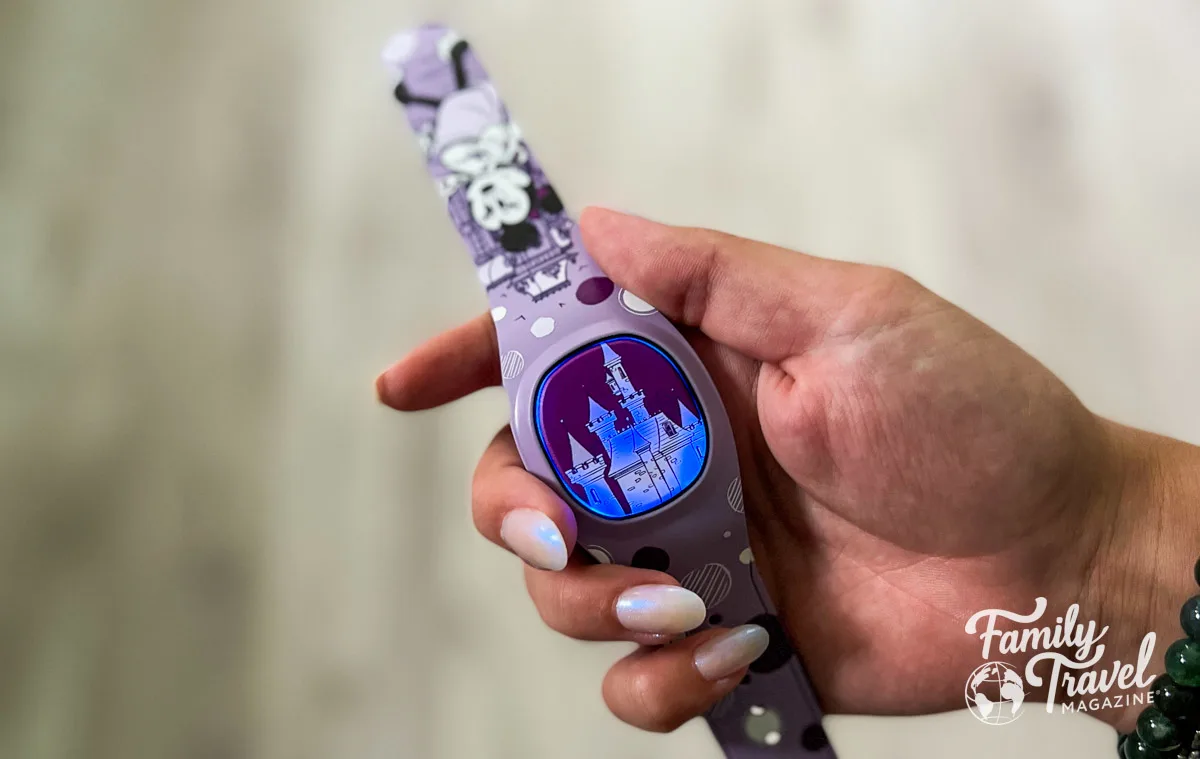 Hand holding a purple Minnie MagicBand with castle lit up