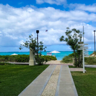 Path leading to beach with turquoise waters, beach chairs, and umbrellas