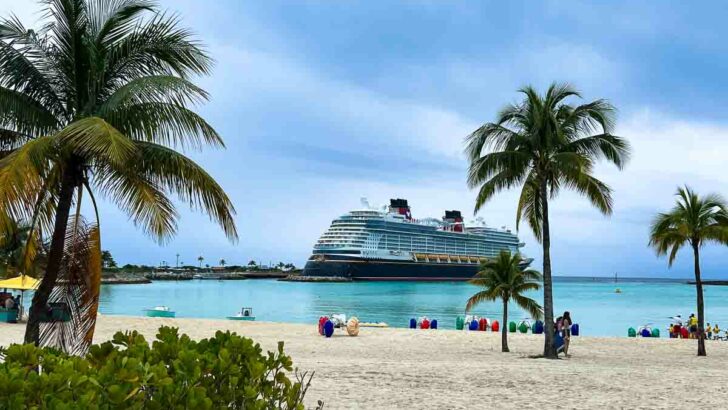 The Disney Wish docked at Castaway Cay with palm trees and water trikes in the foreground.