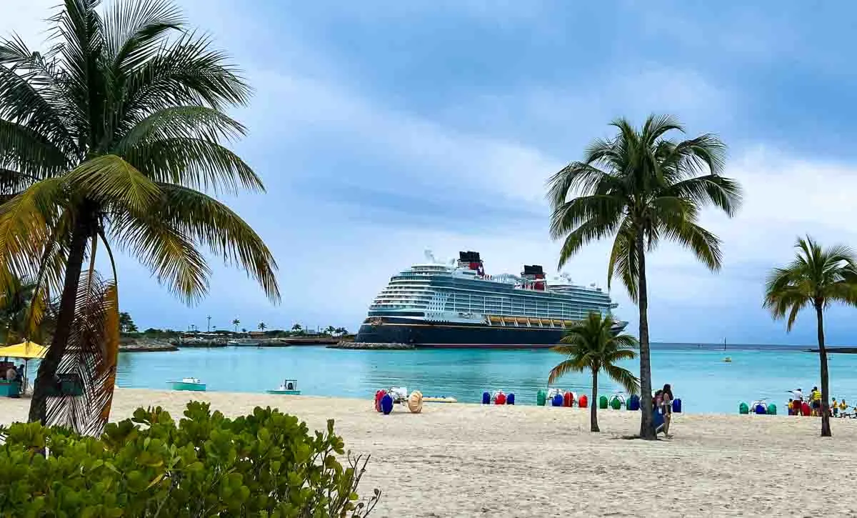 The Disney Wish docked at Castaway Cay with palm trees and water trikes in the foreground.