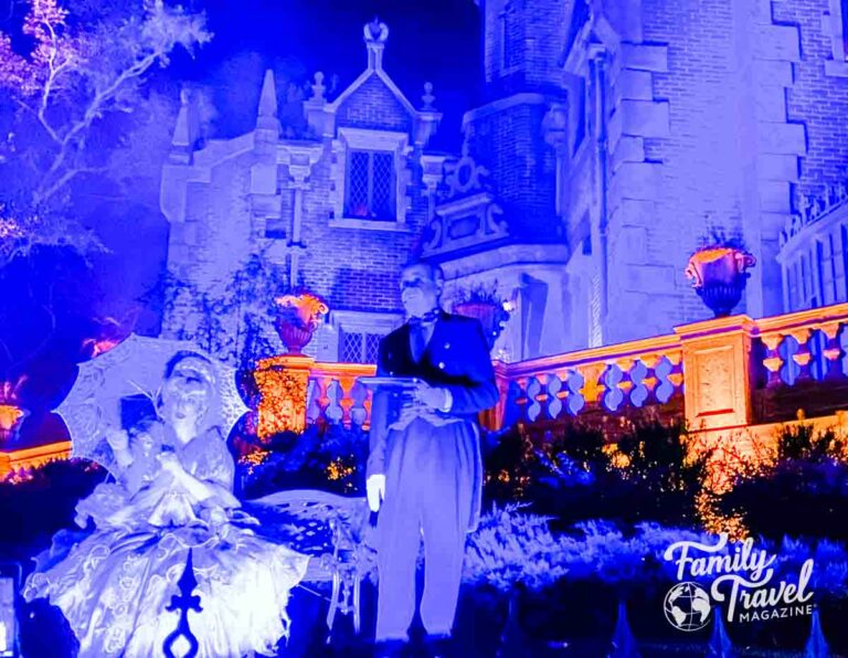 Spooky blue light at Haunted Mansion with butler and woman in dress with umbrella in the front.