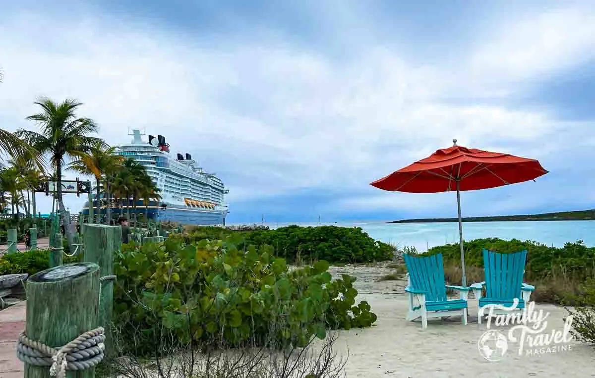 two chairs on beach with umbrella in front of cruise ship