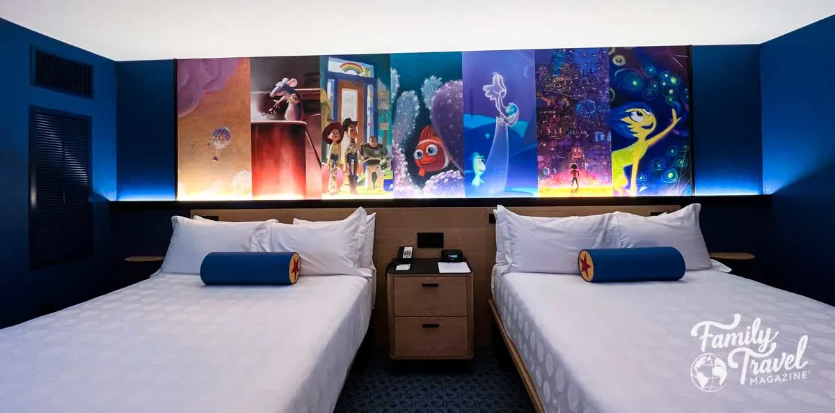 Two queen beds in a hotel with a Pixar themed mural above.