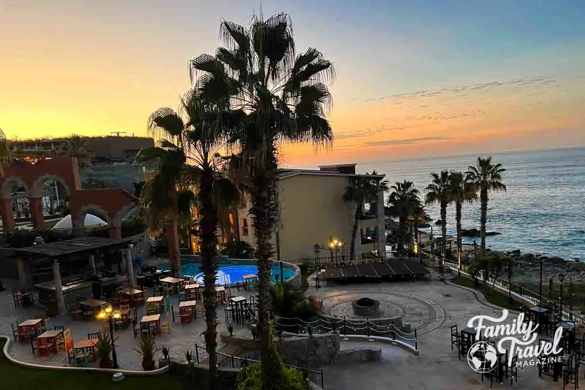 View of resort building and waterfront at sunrise with pools and palm trees