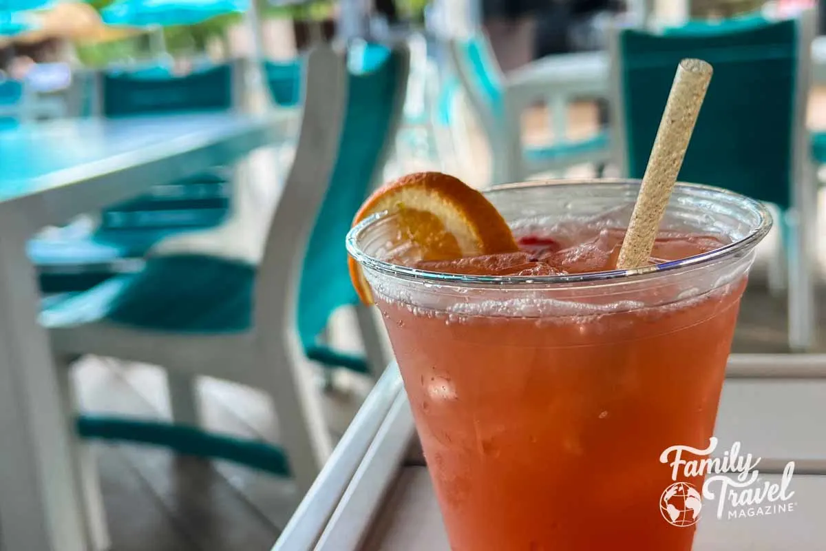 Orange drink in foreground and aqua deck furniture in background