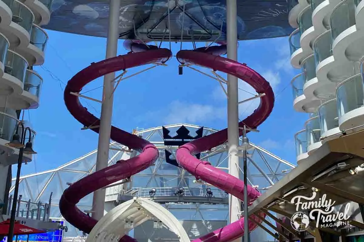 two large purple slides in front of AquaTheater with balcony staterooms overlooking them