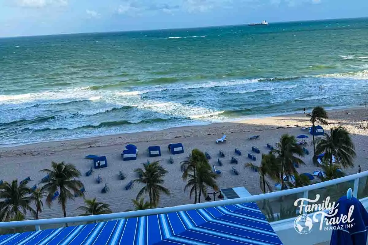 view of the beach from above with loungers, chairs, and palm trees