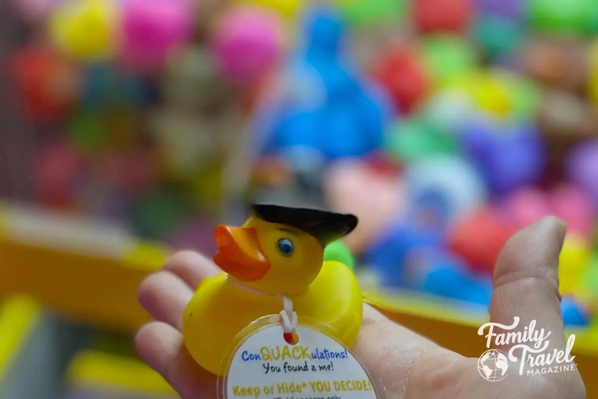 Rubber duck with black hat and tag in front of a colorful claw machine