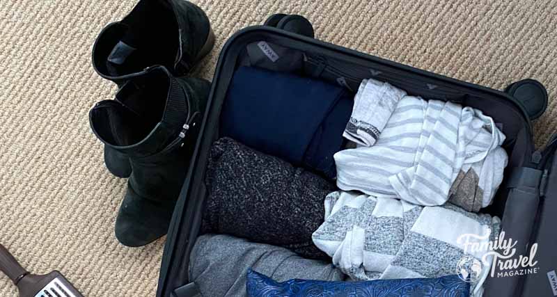 Rolled clothes in a suitcase with black boots beside it